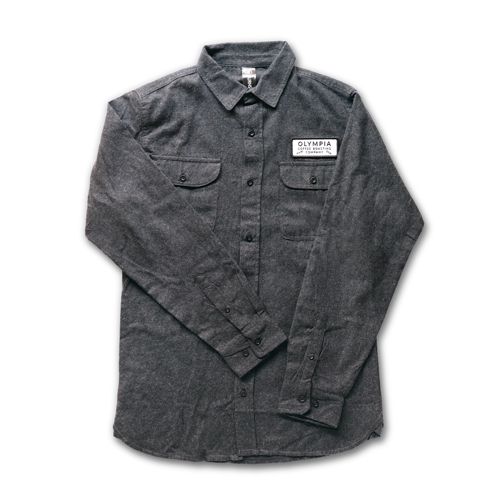 Charcoal grey button front flannel shirt with two button flap pockets on the chest. Over the left chest pocket is a white, rectangular patch embroidered with, "PNW/USA/Olympia Coffee Roasting Company."